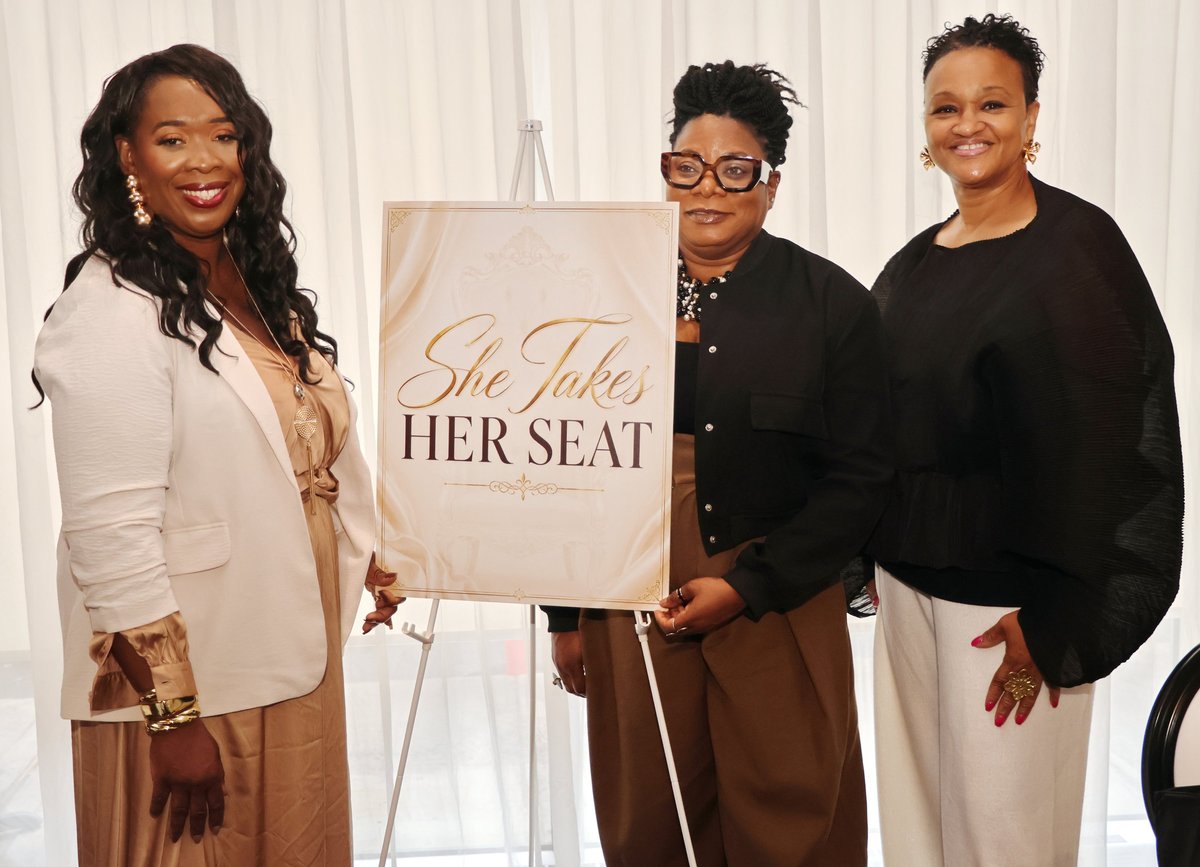 Latoya Belfon and guests beside the She Takes Her Seat event sign